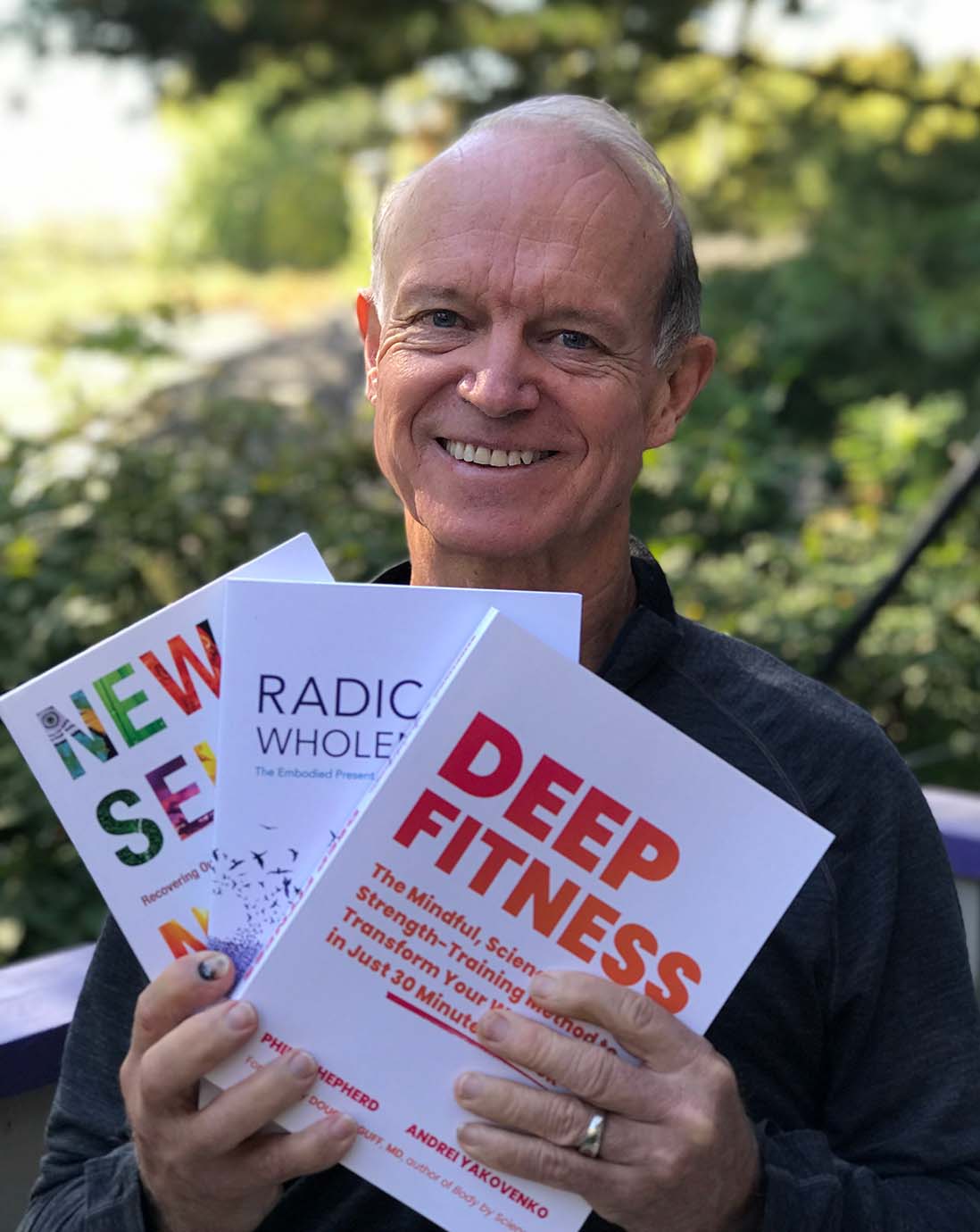 Philip Shepherd, creator and co-director of the Embodied Present Process, fanning out his three books and smiling.